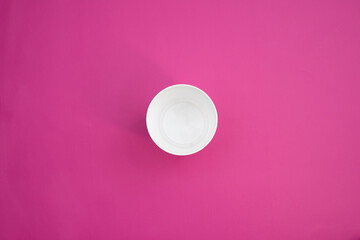 a single white cup isolated on a pink background. utensil shot from top point of view. disposable dishware for graphics and mockup use.