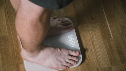 Man step on digital glass scales to check weight. Male weighting on floor scales in domestic room,...