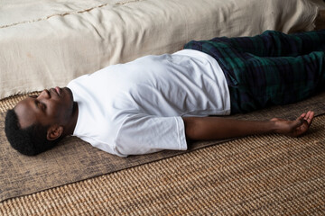 Yoga. African young man meditating on a floor and lying in Shavasana pose.