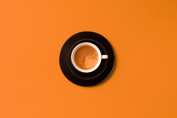 Fresh black hot tasty coffee in white cup on black plate with orange flat lay background.
