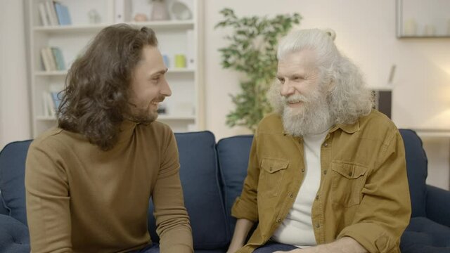 Smiling senior father talking with grownup son at home, trustful relationship