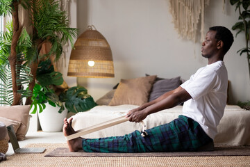 African young man sitting in paschimottanasana or Intense Dorsal Stretch pose, seated forward bend...