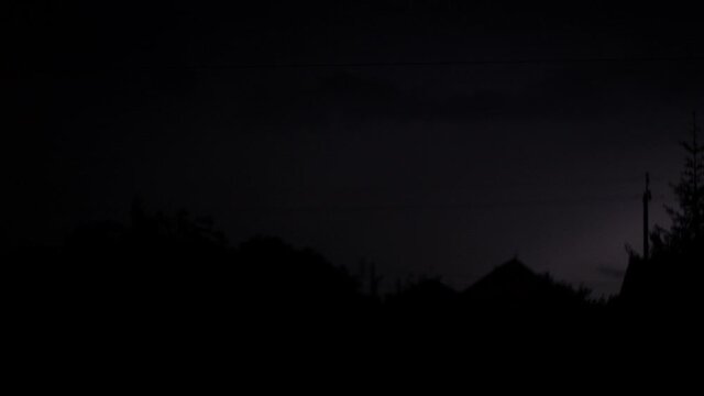 4K video. Flashing lightnings, rain and hail at night. Dramatic electric lightning bolt in the village. Silhouette of houses and trees. Poles with wires, power lines. Extreme weather and thunderstorm