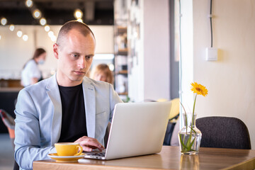 Naklejka na ściany i meble Young successful businessman sitting at coffee in a cafe and working on his laptop.
