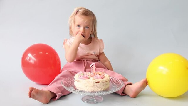 little beautiful blue-eyed girl celebrates her first birthday in the style smash a cake and she tastes her first birthday cake