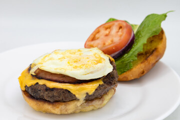 Open Faced American Style Cheeseburger with a Fried Egg and Lettuce and Tomatoes on a White Plate