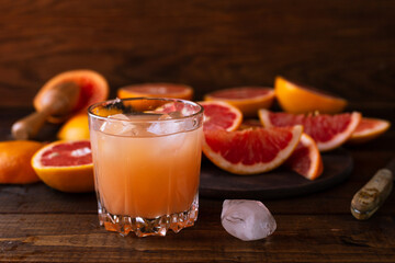 sliced pieces of grapefruit lie on the table on the dark wooden countertop. next to it is a glass of freshly squeezed grapefruit juice