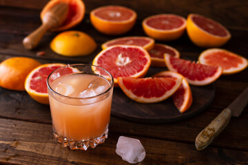 sliced pieces of grapefruit lie on the table on the dark wooden countertop. next to it is a glass of freshly squeezed grapefruit juice