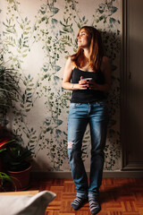 Fototapeta na wymiar Young red-haired girl with a cup standing near the window enjoying relaxing at home