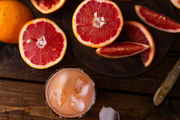 sliced pieces of grapefruit lie on the table on the dark wooden countertop. next to it is a glass of freshly squeezed grapefruit juice