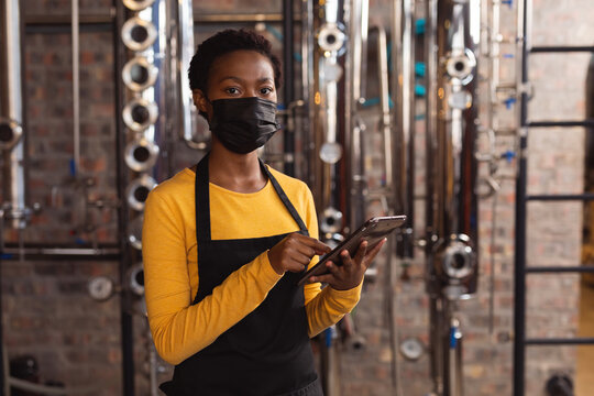 Portrait of african american female worker wearing face mask using digital tablet at gin distillery