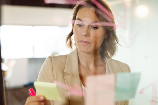 Caucasian businesswoman making notes and adding post-ins on transparent board