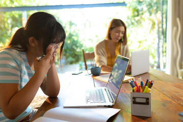 Asian girl using laptop, learning online her mum working in background