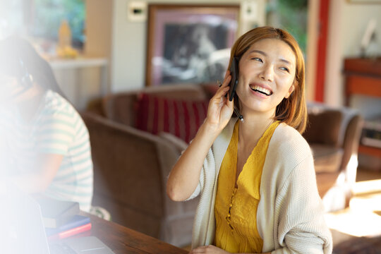 Smiling asian woman talking on smartphone, working from home