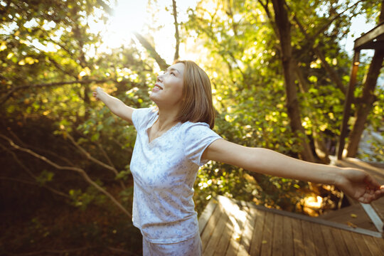 Smiling asian woman in pyjamas with her arms outstretched in garden