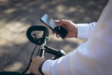 Midsection of asian businessman using smartphone standing with bike in city street