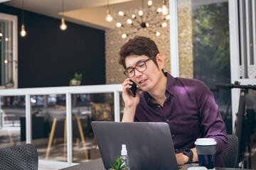 Asian businessman using smartphone and laptop in hotel lobby