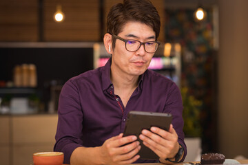 Asian businessman using tablet and wireless earphones in cafe