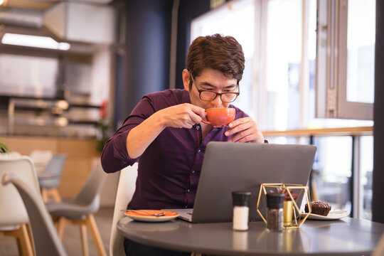 Asian businessman using laptop drinking coffee in cafe