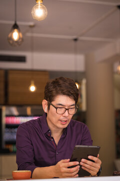 Asian businessman using tablet and wireless earphones in cafe