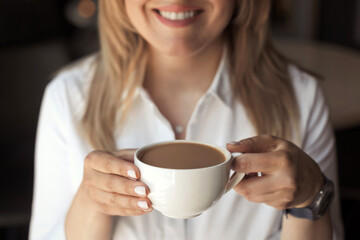 Closeup woman's hand holding a white cup of coffee with milk in coffee house