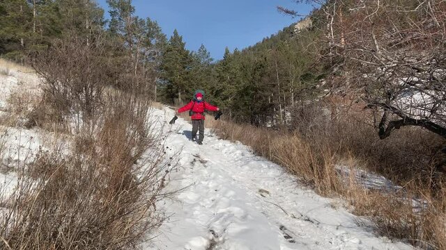 A girl with a large teristic backpack descends from the mountain along a snow-covered trail. Winter hike