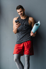 Young white sportsman using cellphone while standing with mat