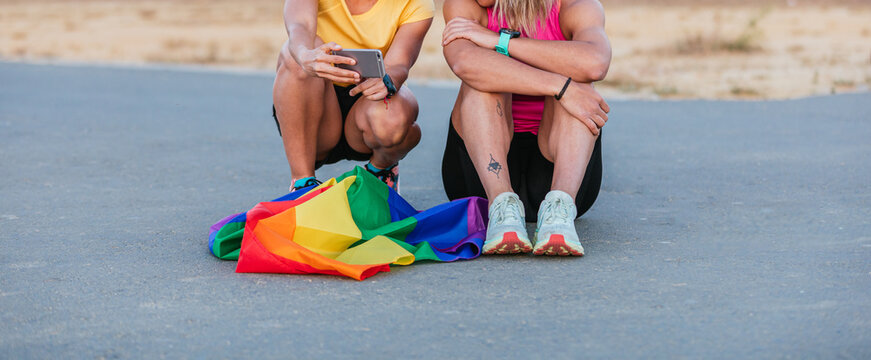 Lesbian couple looking at smartphone with rainbow flag. Unrecognizable. Gay pride.