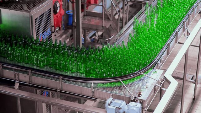 line for filling beer in a brewery. Empty green glass bottles moving on a conveyor belt in a queue at a beer factory.