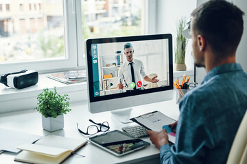 Serious young man talking to collegue by video call while sitting in office