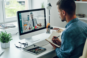 Confident young man talking to collegue by video call while sitting in office