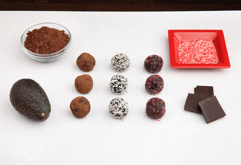 variety of healthy cacao truffle snacks on white tabletop showing ingredients including avocado and sprinkles