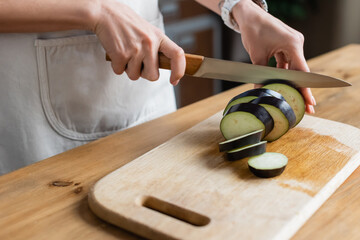 close up view of female hands cutting eggplant on chopping board in kitchen - Powered by Adobe
