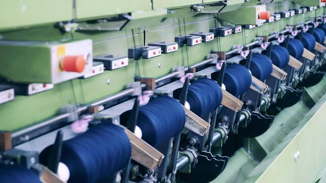 Spools with threads are spinning in the factory machine