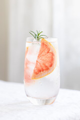 Glass of cold water with grapefruit and rosemary garnish.