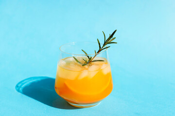 Refreshing cocktail with orange and rosemary sprig on a blue background. Summer drinks. Copy space