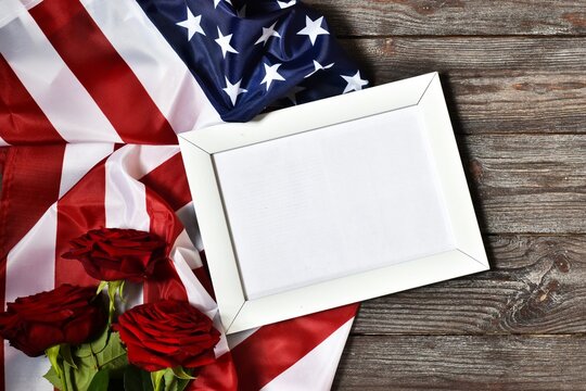 Independence Day USA concept. Memorial Day. Red roses with USA flag and white frame on a dark wooden background. top view, flat lay. Copy space.
