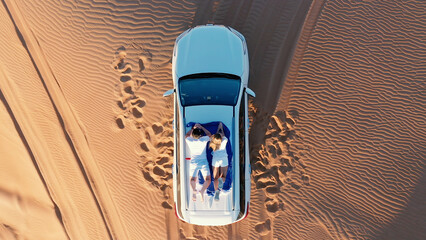 AERIAL. Top view of young couple relaxing on the car's roof at the desert. © skymediapro