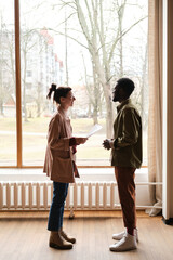 Young people discussing report together while standing against the big window