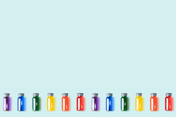 Pattern of glass vials with rainbow-coloured liquid on blue background.Vaccine and covid concept. copy space.