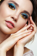 Closeup macro shot of human female face with hands near face, yellow liner and blue eyes shadows makeup.