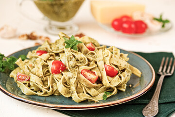 Fettuccine pasta with sauce pesto, cherry tomatoes, pine nuts and parmesan cheese on concrete background. Selective focus.
