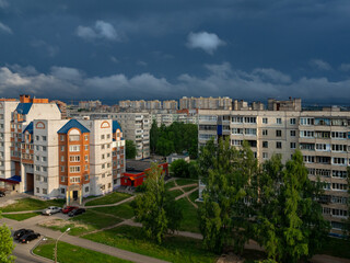 Fototapeta na wymiar Sunrise at the residential area of the Cheboksary city with dark blue storm sky and clouds, sun rays and buildings.