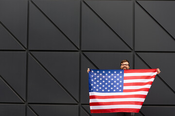 Young handsome man holding a USA flag and standing against the wall