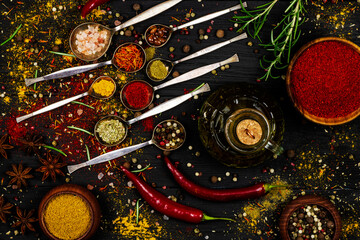 An assortment of oriental spices in iron spoons scattered on a black wooden surface as a background.