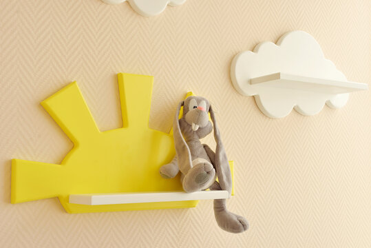 close-up Stylish and modern Interior design. Home for the child room. Children's shelves in the form of white clouds on a plain beige wall with yellow photo frame and a gray hare