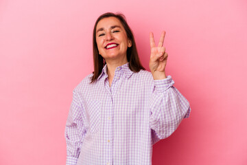 Middle age caucasian woman isolated on pink background joyful and carefree showing a peace symbol with fingers.