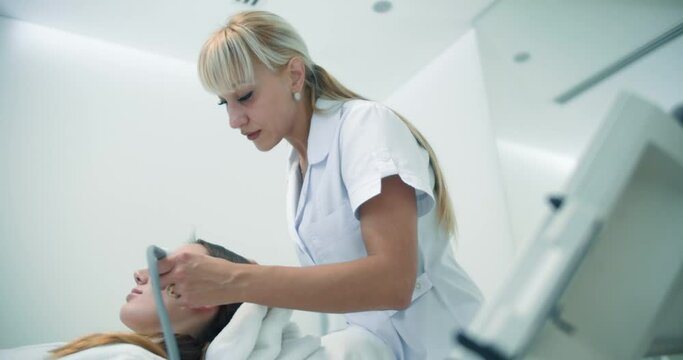 A female cosmetologist is using the Dermadrop TDA device for doing a non-injection bio-revitalization procedure for the female client who is laying in the cosmetology bed.