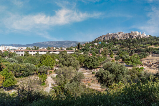 Ancient Agora of Athens archaeological site panoramic view. Stoa of Attalus (left), Acropolis rock (right) in the background. Athens, Attica, Greece. Sunny day, cloudy blue sky