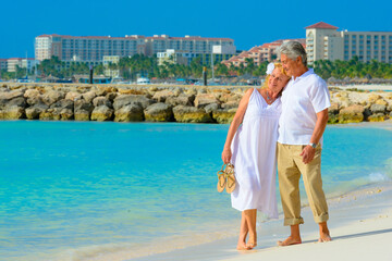 Fototapeta na wymiar Older couple walking on the beach in Aruba dressed in white outfits